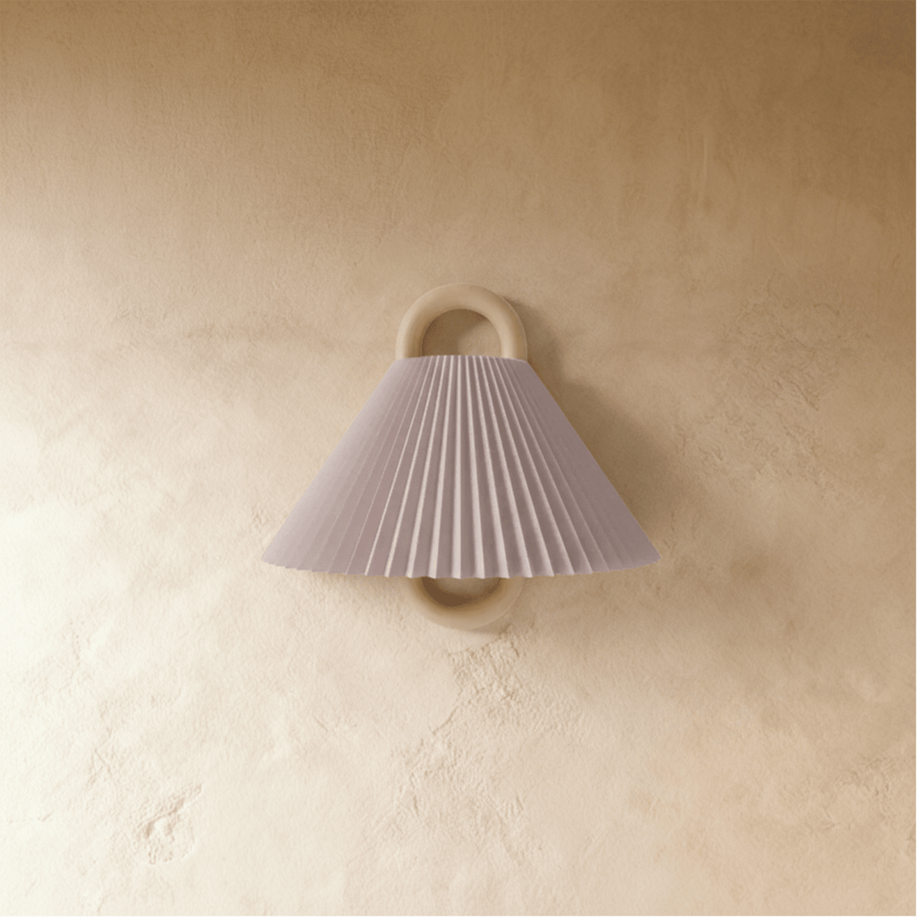 Clérachic wall light with a pleated blush pink fabric shade on a wood ring mount, unlit against a warm plaster wall.