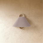 Clérachic wall light with a pleated blush pink fabric shade on a wood ring mount, unlit against a warm plaster wall.