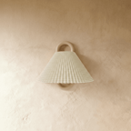 Clérachic wall light with a pleated sage and cream striped fabric shade on a wood ring mount, unlit against a plaster wall.