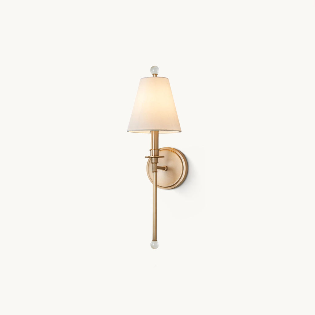 Gold-toned Clérachic wall light with a tapered white fabric shade and a clear glass ball finial, on a plain off-white backdrop.