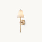 Gold-toned Clérachic wall light with a tapered white fabric shade and a clear glass ball finial, on a plain off-white backdrop.