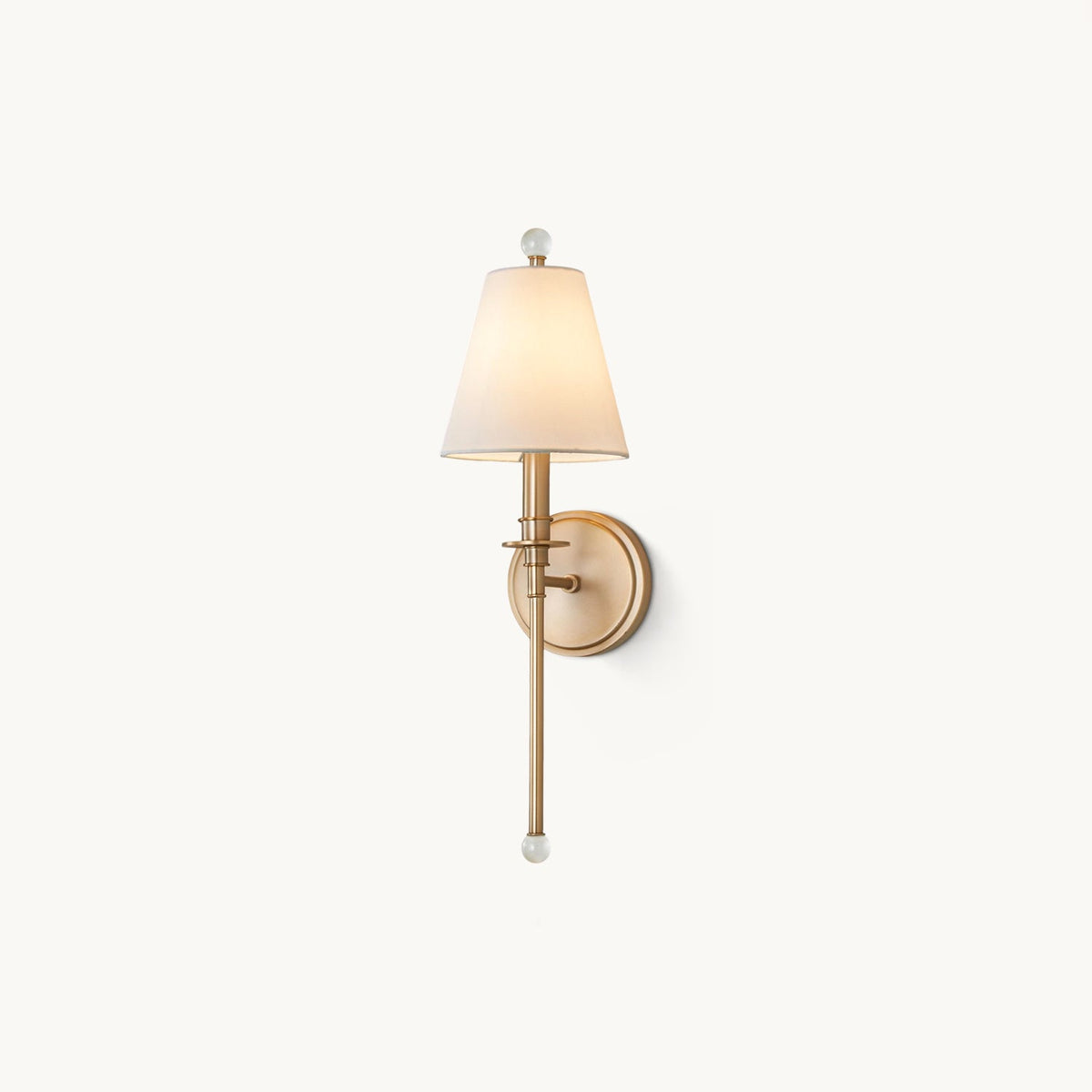 Gold-toned Clérachic wall light with a tapered white fabric shade and a clear glass ball finial, on a plain off-white backdrop.
