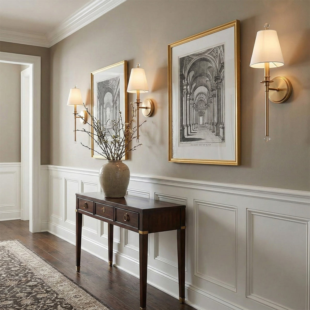 Clérachic sconces with gold-toned arms in an entry hall, hung beside framed architectural prints above a dark console table.