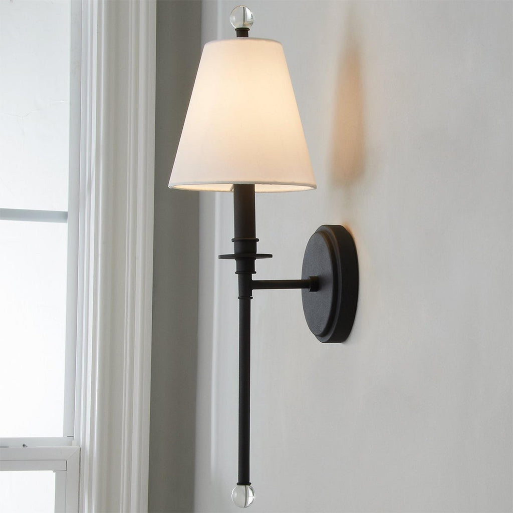 Black version of this Clérachic wall light with a white tapered shade and round backplate, seen close up beside a white window frame.