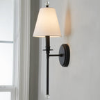Black version of this Clérachic wall light with a white tapered shade and round backplate, seen close up beside a white window frame.