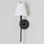 Unlit white shade on a black Clérachic sconce, the long slim rod ending in a clear glass ball, against a light grey wall.
