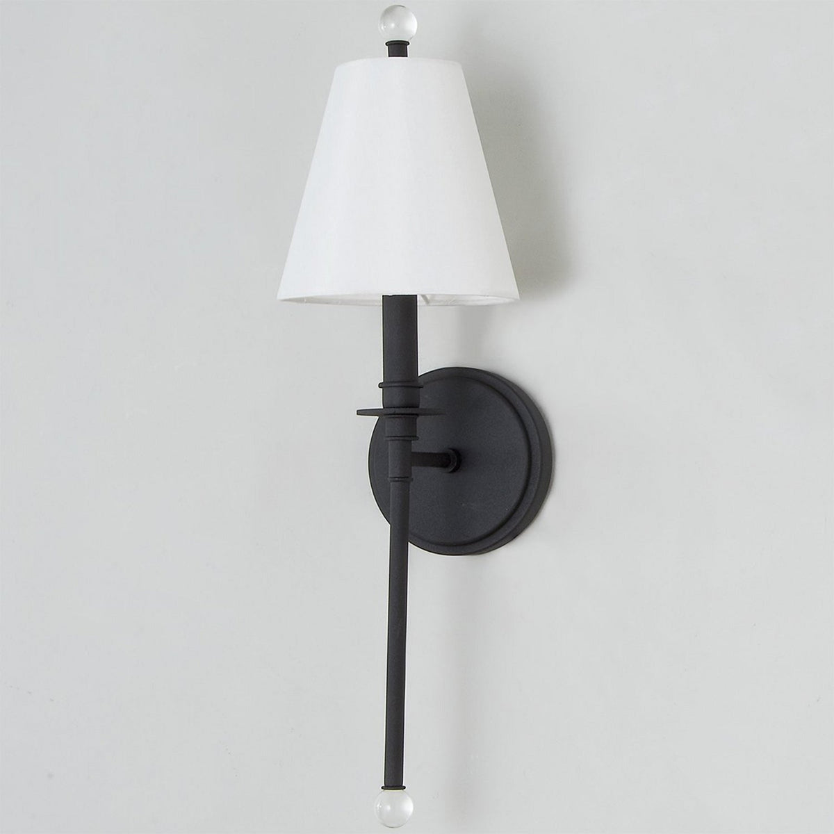Unlit white shade on a black Clérachic sconce, the long slim rod ending in a clear glass ball, against a light grey wall.