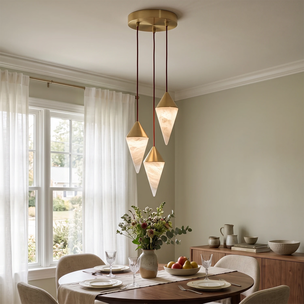 Three faceted alabaster drops on this Clérachic chandelier hang above a round table set for dinner near a window.