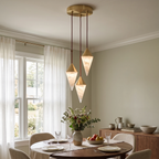 Three faceted alabaster drops on this Clérachic chandelier hang above a round table set for dinner near a window.