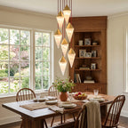 Five brass-capped alabaster drops on this Clérachic chandelier hang above a wooden dining table before a book-lined hutch.