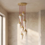 Brass-capped alabaster drops on this Clérachic chandelier hang in a sunlit plastered corner, casting long shadows.