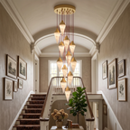 A grand stairwell hung with framed prints holds this Clérachic chandelier's tall cluster of brass-capped drops.