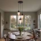 Autumn trees show through the window behind two black-capped drops on this Clérachic chandelier, over a round table.