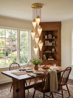 Daylight streams through a tall window onto this Clérachic chandelier's brass-capped drops above a dining table.