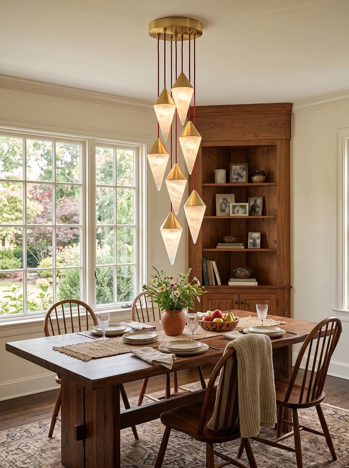 Daylight streams through a tall window onto this Clérachic chandelier's brass-capped drops above a dining table.