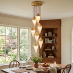 This Clérachic chandelier's brass-capped drops glow warm above a dining table beside a wood hutch and window.