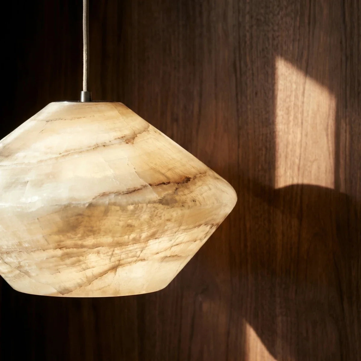 Close detail of the Clérachic alabaster pendant shade, with honey bands of veining lit warm against walnut panelling.