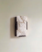 Clérachic single alabaster wall light with a dark bronze metal frame, unlit, mounted on a soft sage wall