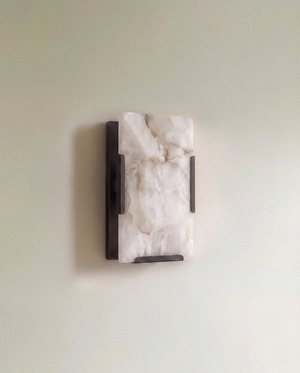Clérachic single alabaster wall light with a dark bronze metal frame, unlit, mounted on a soft sage wall
