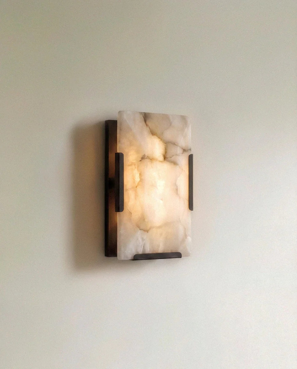Clérachic single alabaster wall light in dark metal, lit, the veined stone glowing warmly against a pale wall