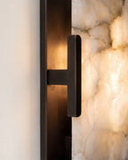Close view of the Clérachic alabaster wall light's dark metal T-bracket holding the glowing, cloudy stone panel