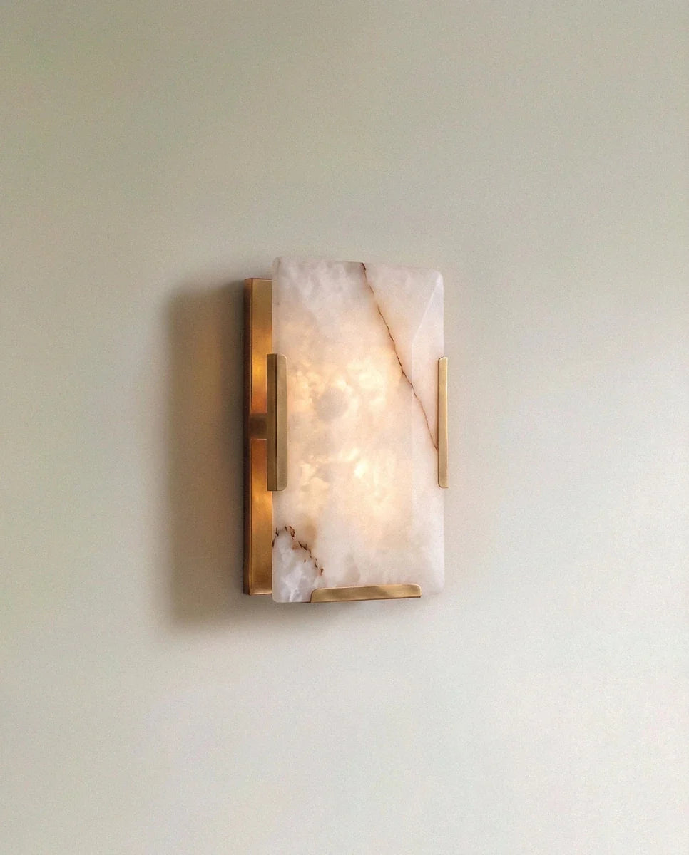 Clérachic single alabaster wall light in lacquered brass, lit, warm light glowing through the white veined stone