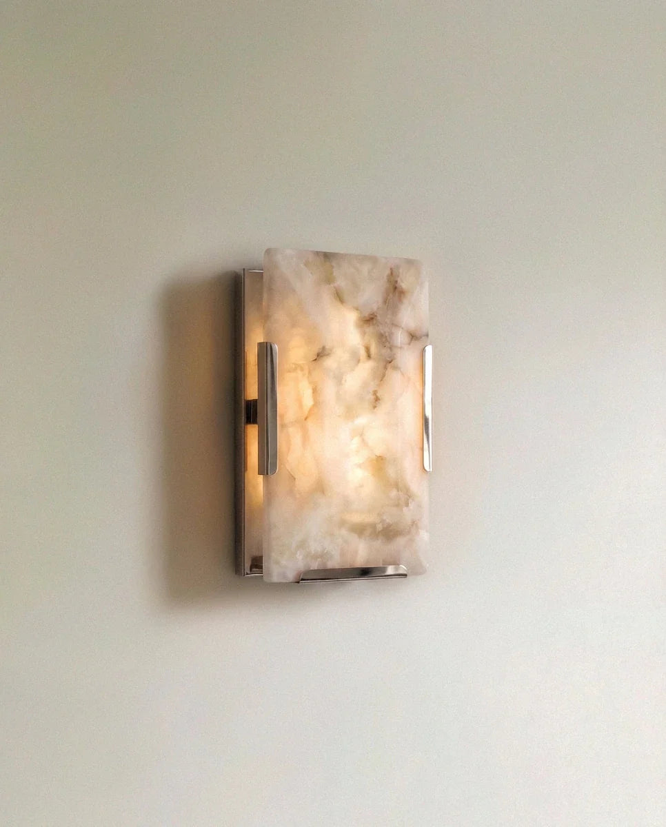 Clérachic single alabaster wall light with a polished steel frame, lit, amber veining glowing in the stone panel