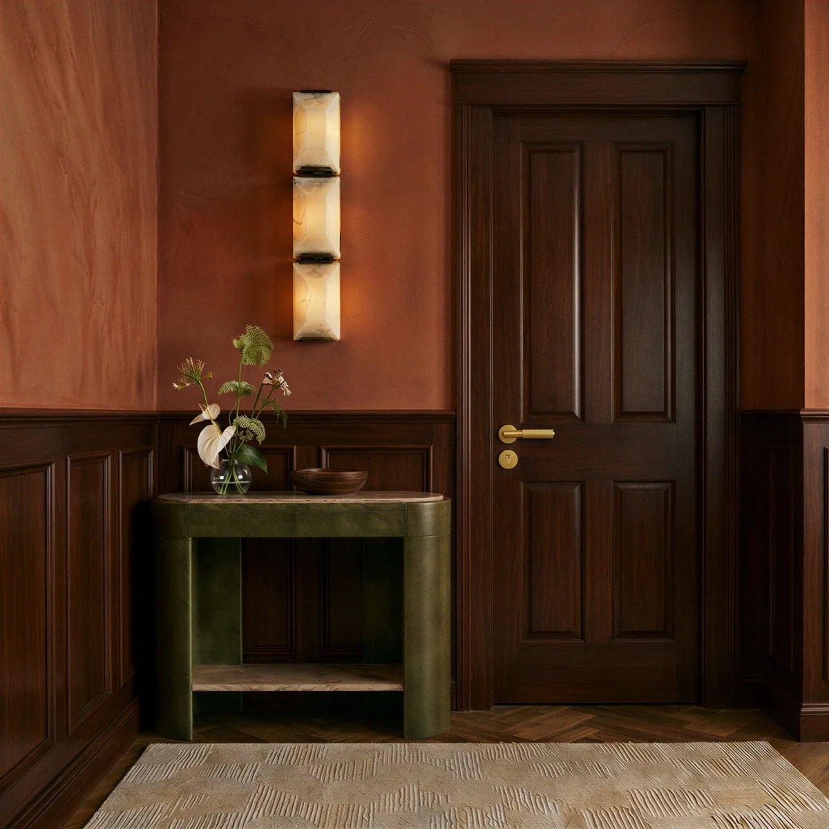 Clérachic three-panel alabaster wall light on a terracotta hallway wall beside a panelled door and a green console