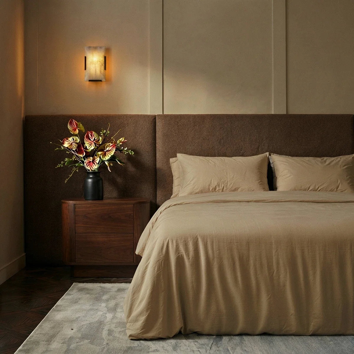 Clérachic single alabaster wall light glowing above a walnut bedside cabinet and an upholstered bed in warm neutrals
