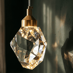 Close view of a Clérachic faceted crystal pendant light, its brushed gold cap and cut glass catching warm light against a dark wall.