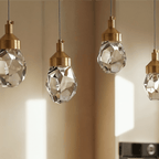 Close crop of Clérachic faceted crystal pendant lights in a row, brushed gold caps and cut facets in soft window light.