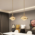 Two faceted amber glass pendants on slim gold rods hang under a lit ceiling edge above a white dining table, from Clérachic.
