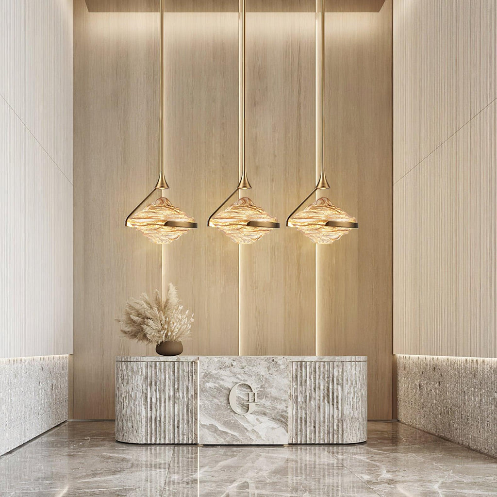 Three faceted amber glass pendants on slim gold rods glow in a row above a marble console with dried grasses, from Clérachic.