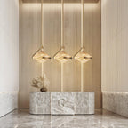 Three faceted amber glass pendants on slim gold rods glow in a row above a marble console with dried grasses, from Clérachic.