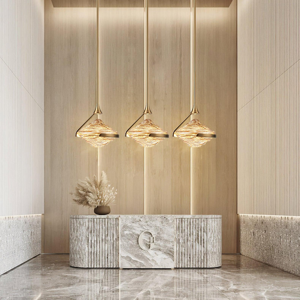 Three faceted amber glass pendants on slim gold rods glow in a row above a marble console with dried grasses, from Clérachic.