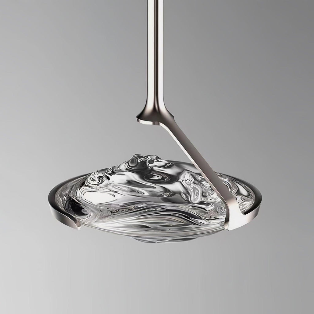 Close view of a rippled clear glass shade held by a silver curved arm and slim rod against a grey backdrop, a Clérachic pendant.