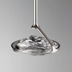 Close view of a rippled clear glass shade held by a silver curved arm and slim rod against a grey backdrop, a Clérachic pendant.