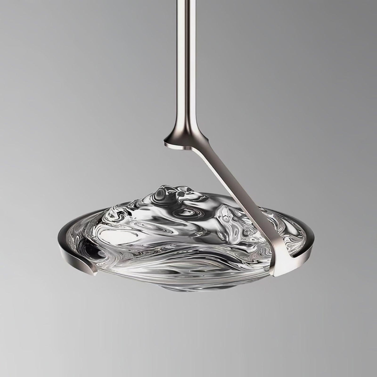 Close view of a rippled clear glass shade held by a silver curved arm and slim rod against a grey backdrop, a Clérachic pendant.