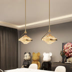 Two faceted amber glass pendants on gold rods hang beneath a lit cove ceiling above a white table and bright chairs, from Clérachic.