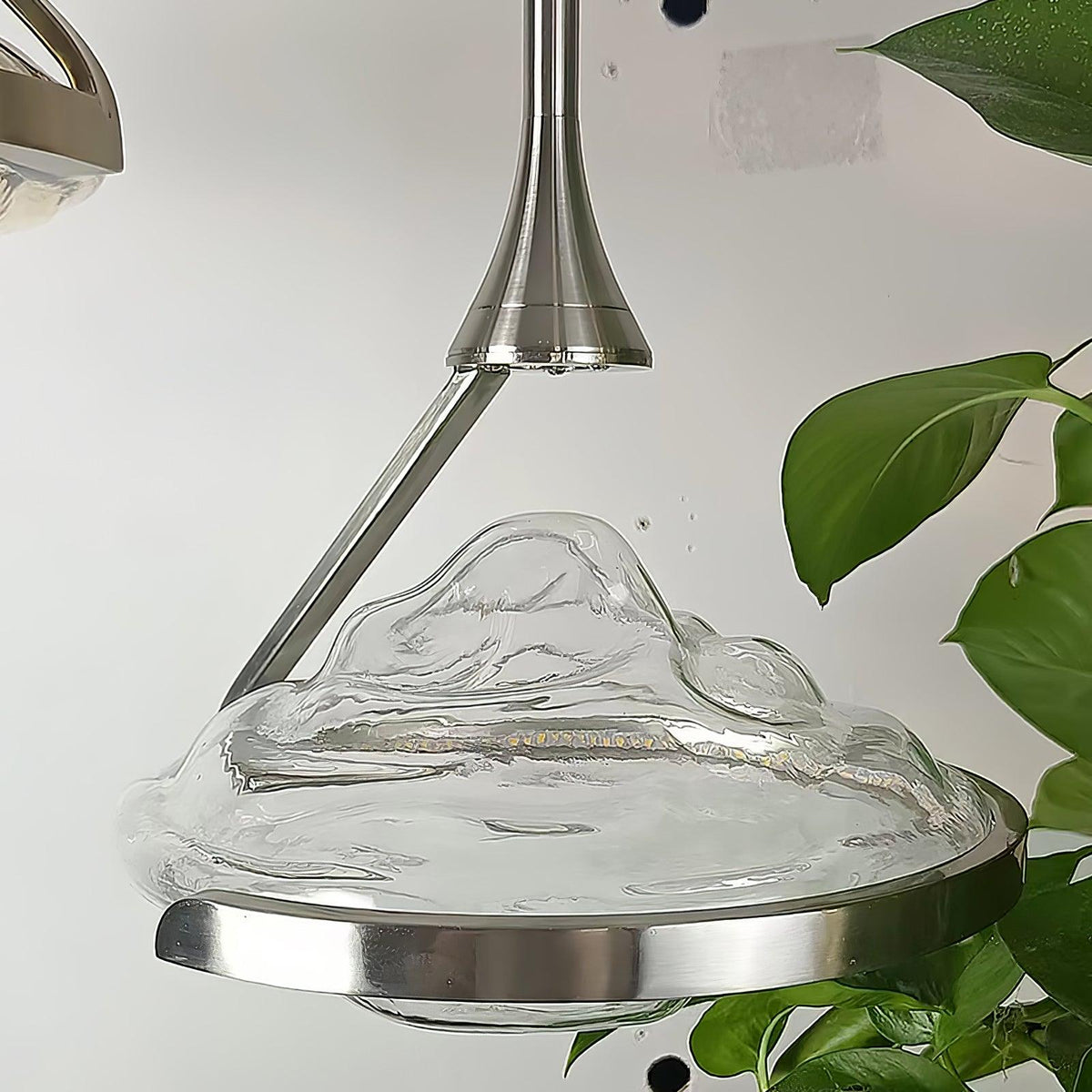 Close view of a rippled clear glass shade with a silver ring and arm, a green leaf at the edge, on this Clérachic pendant.