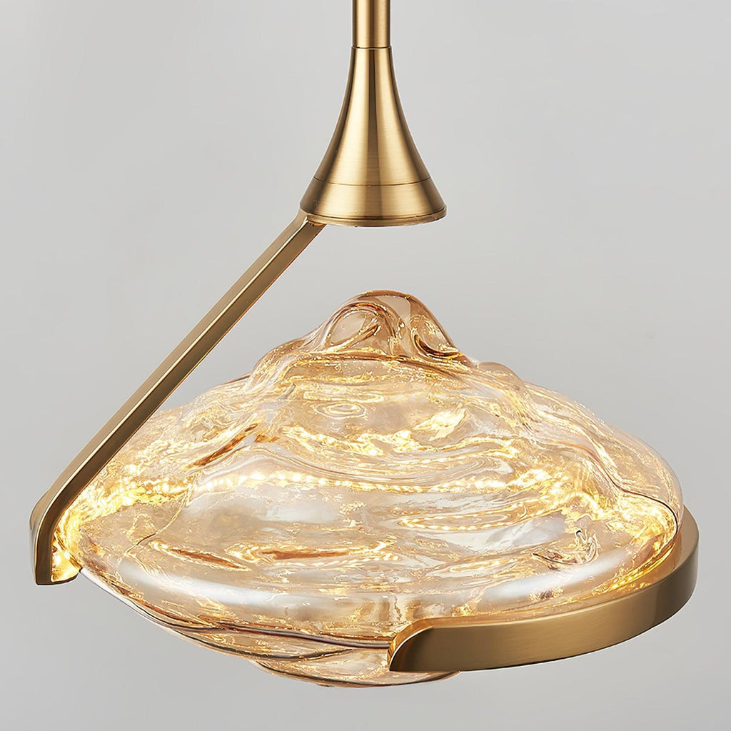 A lit faceted amber glass shade with a gold ring is seen from slightly below, with the flared gold joint above, from Clérachic.