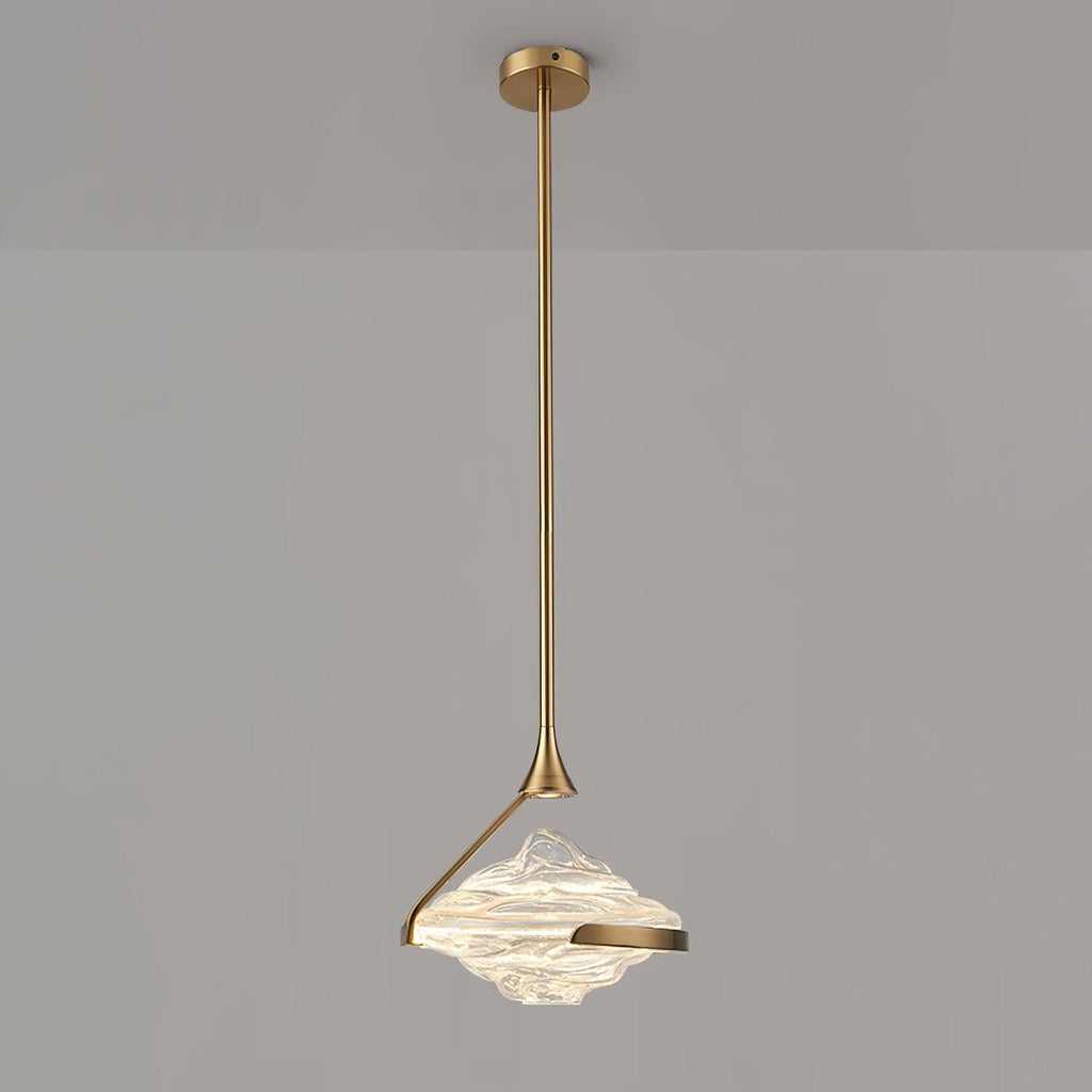 A faceted clear glass pendant with a gold arm and rod hangs against a grey wall, lit white, from Clérachic.