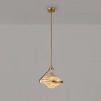 A faceted amber glass pendant with a gold arm and ceiling plate hangs against a grey wall, glowing warm, from Clérachic.