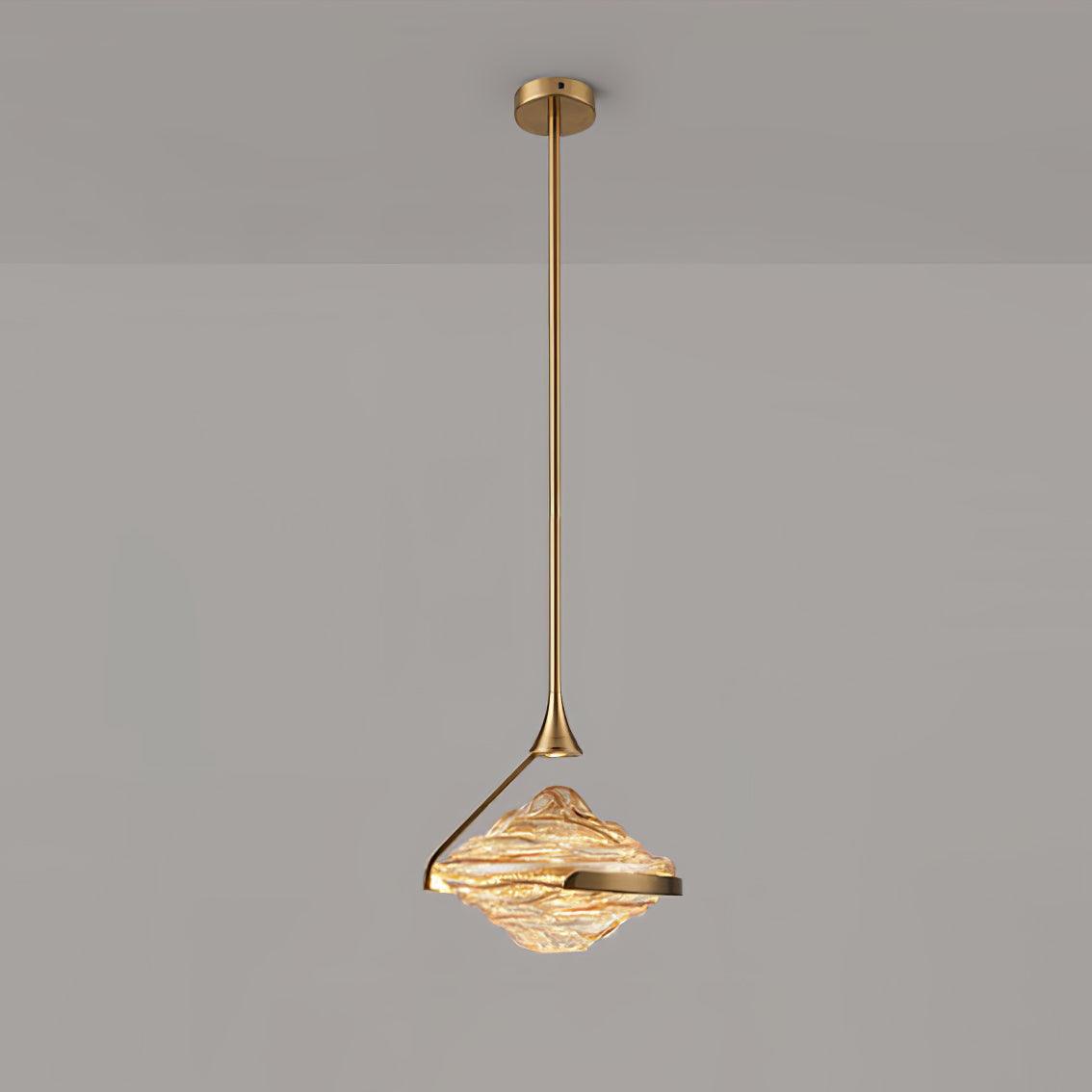 A faceted amber glass pendant with a gold arm and ceiling plate hangs against a grey wall, glowing warm, from Clérachic.