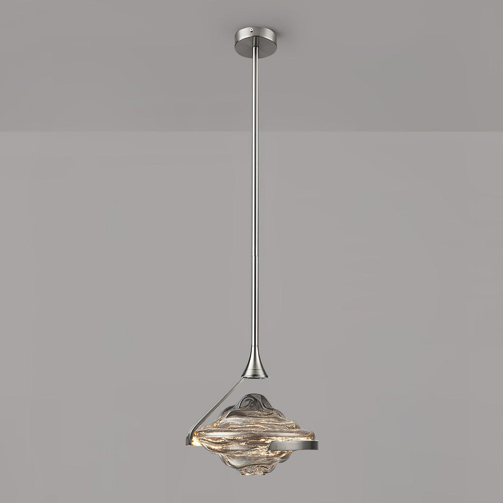 A faceted pendant with a smoke grey top and amber lit glass hangs from a chrome rod against a grey wall, from Clérachic.