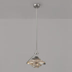 A faceted pendant with a smoke grey top and amber lit glass hangs from a chrome rod against a grey wall, from Clérachic.