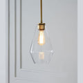 Clérachic faceted glass pendant light in clear glass, the slim teardrop shade lit beside a white panelled wall.