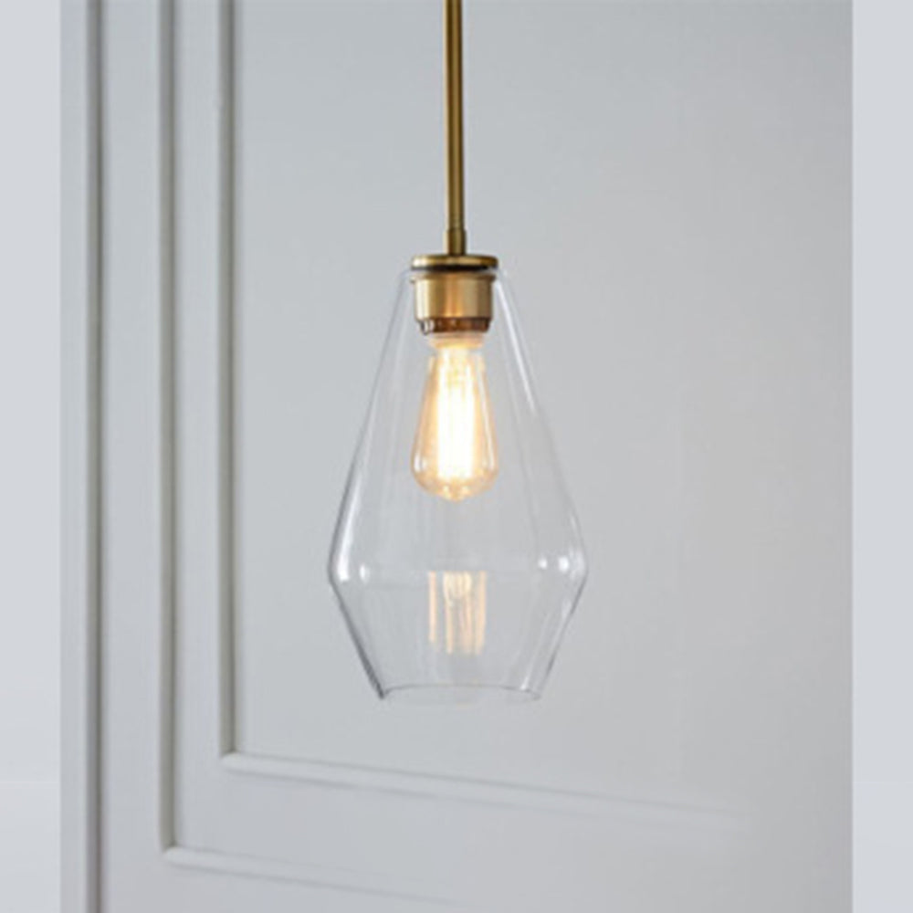 Clérachic faceted glass pendant light in clear glass, the slim teardrop shade lit beside a white panelled wall.