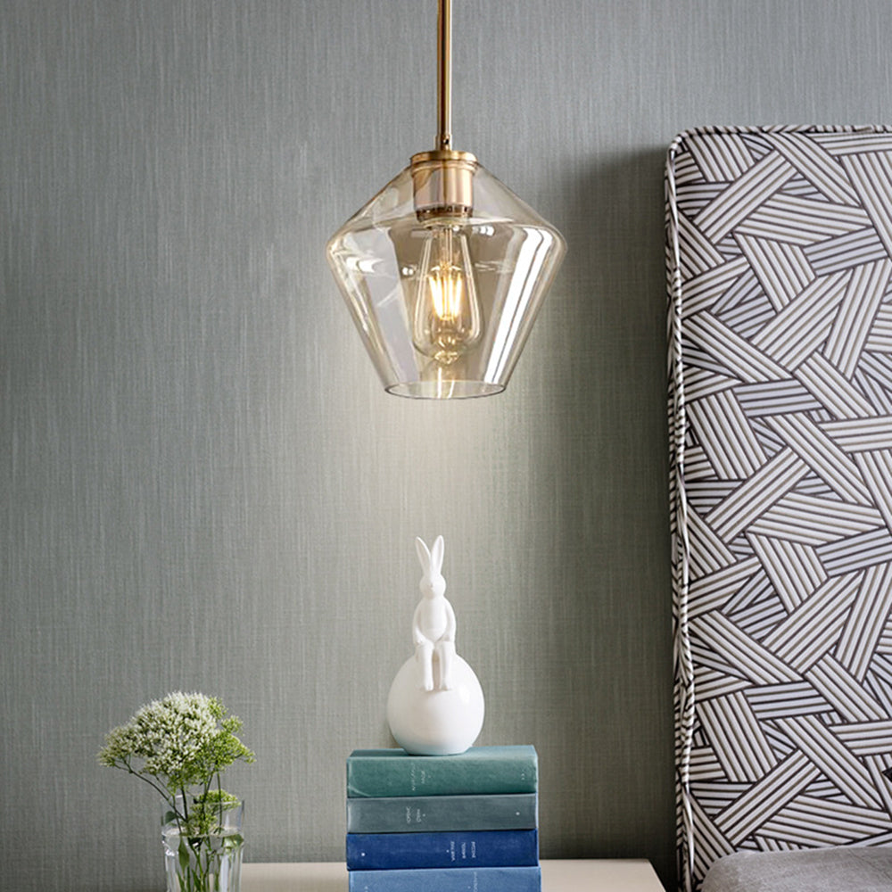 Clérachic faceted glass pendant light in amber hung low beside a bed, lighting books and a small ceramic rabbit.