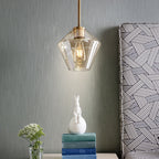 Clérachic faceted glass pendant light in amber hung low beside a bed, lighting books and a small ceramic rabbit.